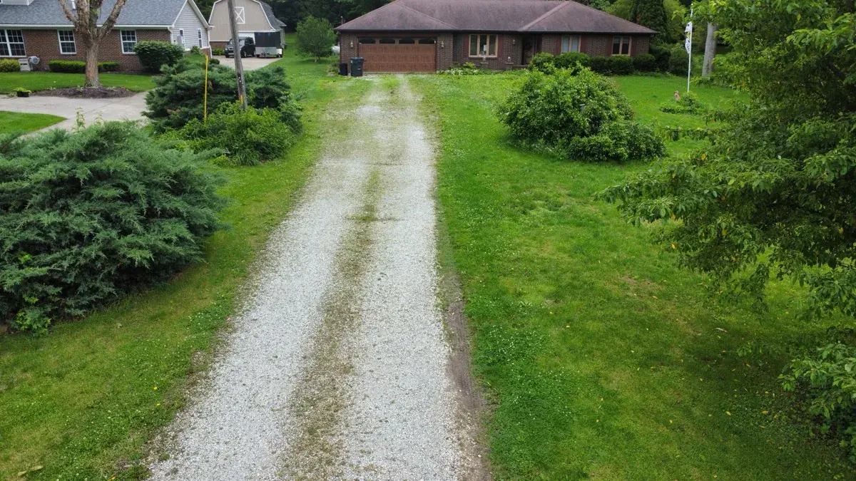 A worn gravel driveway with grass growing through the thin, patchy surface
