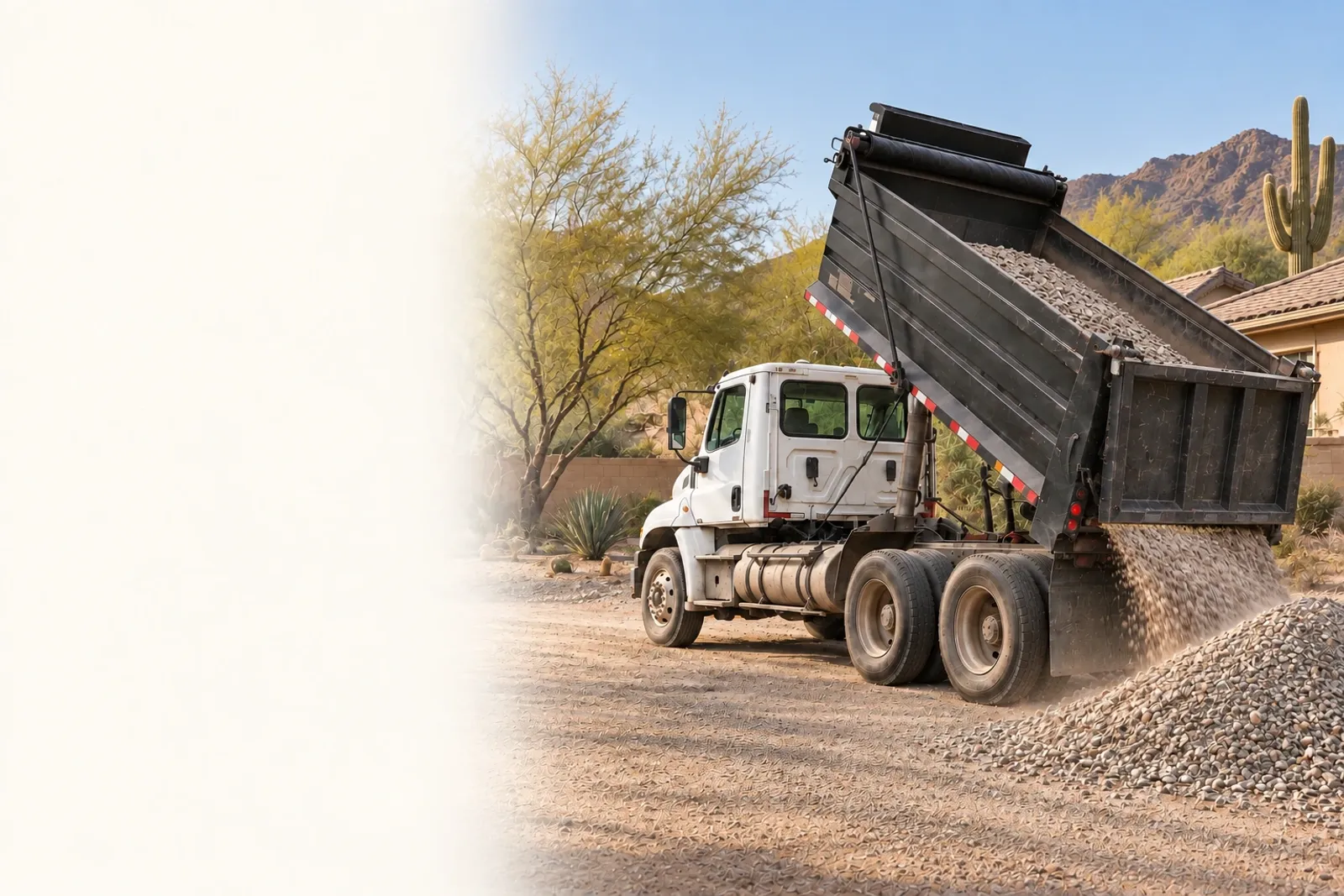 A dump truck tipping a load of gravel in front of a desert-landscaped home, with a saguaro cactus and mountains behind