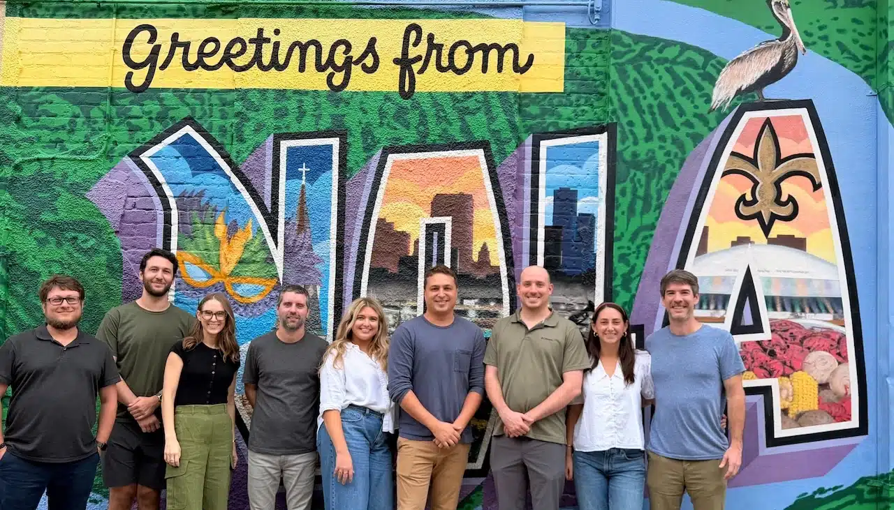 Team photo of the HelloGravel crew standing in front of a colorful “Greetings from NOLA” mural.
